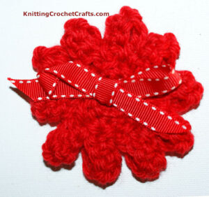 Finished crochet flower embellished with a red and white ribbon bow.